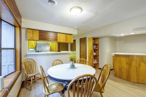 Un comedor con una mesa redonda, sillas de madera y un florero con flores.