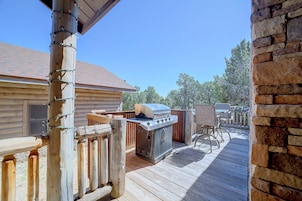 A wooden deck with a barbecue grill, outdoor furniture, and a cabin with a tiled roof.