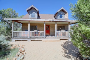 A two-story log cabin with a red door, a porch with wooden railings, and a stone foundation.