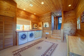Interieur van een blokhut met houten wanden, een wasmachine, een eettafel en een trap.