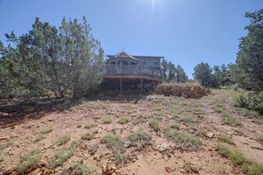 A two-story wooden house with a balcony, surrounded by sparse vegetation and a dry, rocky landscape. - On-site Hiking! Spacious Happy Jack Home w/ Deck (Happy Jack)
