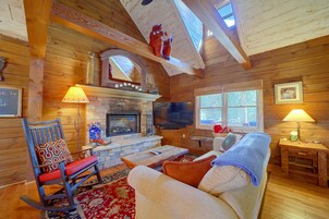 Un acogedor interior de cabaña con chimenea de piedra, paredes de madera, un televisor y un espacio de estar confortable.