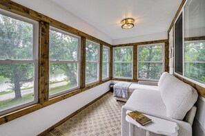 Un coin lecture confortable avec un canapé blanc, une petite table et une grande fenêtre donnant sur une forêt.