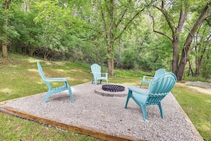 Un espace aménagé avec des fauteuils Adirondack et un foyer, le tout situé dans un cadre boisé.