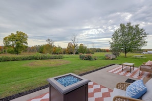 A patio area with a fire feature, outdoor furniture, and a view of a grassy landscape with trees. - 50-acre Hilltop Home: Upstate Getaway (Mooers)