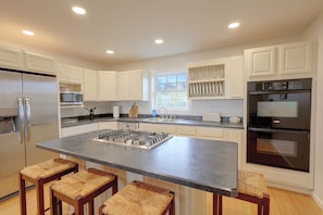A modern kitchen with white cabinets, stainless steel appliances, a central island with stools, and a window providing natural light. - 50-acre Hilltop Home: Upstate Getaway (Mooers)