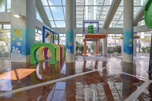An indoor water play area with colorful structures and a caution sign for slippery surfaces. - Ocean-view Dunes Village Condo: Water Park & Pools (Myrtle Beach)