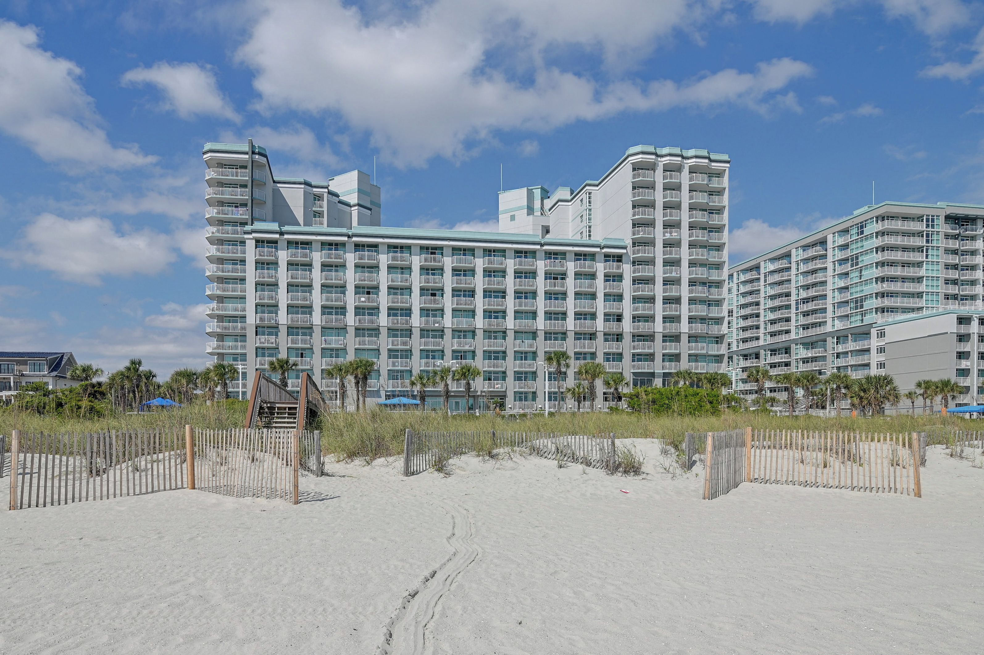 A beachfront hotel with multiple balconies, a sandy beach in the foreground, and a clear sky.