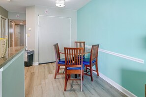 A dining area with a table and chairs, a trash bin, and a door. - Ocean-view Dunes Village Condo: Water Park & Pools (Myrtle Beach)