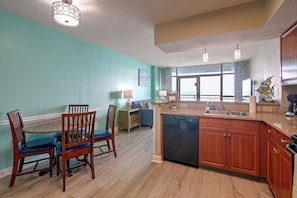 A kitchen with wooden cabinets, a dishwasher, a dining area with chairs, and a view through the window. - Ocean-view Dunes Village Condo: Water Park & Pools (Myrtle Beach)