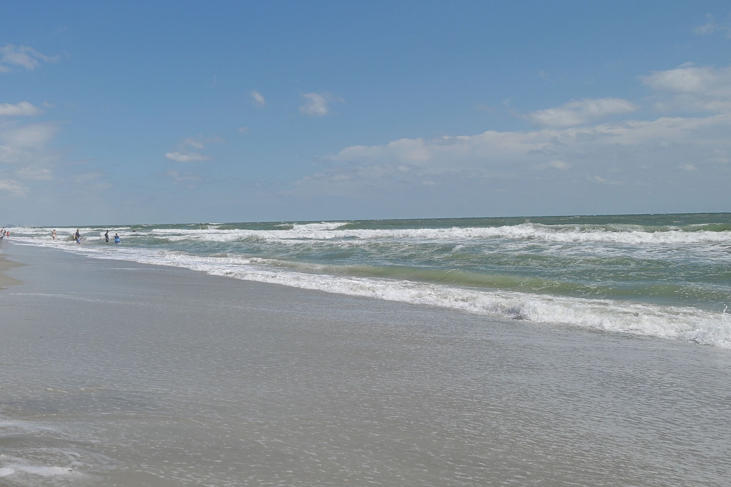 Une plage avec des vagues, un ciel dégagé et quelques personnes.