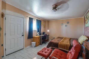 A bedroom with a bed, a desk, a chair, a small table, a waste bin, and a ceiling fan. - Studio 3 Mi to Tucson Airport! Bring Your Pups (Tucson)