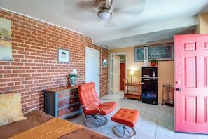 A room with a brick wall, a red door, a wooden dresser, a red chair, a small table, and a ceiling fan. - Studio 3 Mi to Tucson Airport! Bring Your Pups (Tucson)