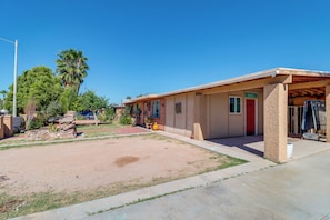 A single-story building with a covered porch, a red door, and a small garden area with a palm tree and rocks. - Studio 3 Mi to Tucson Airport! Bring Your Pups (Tucson)