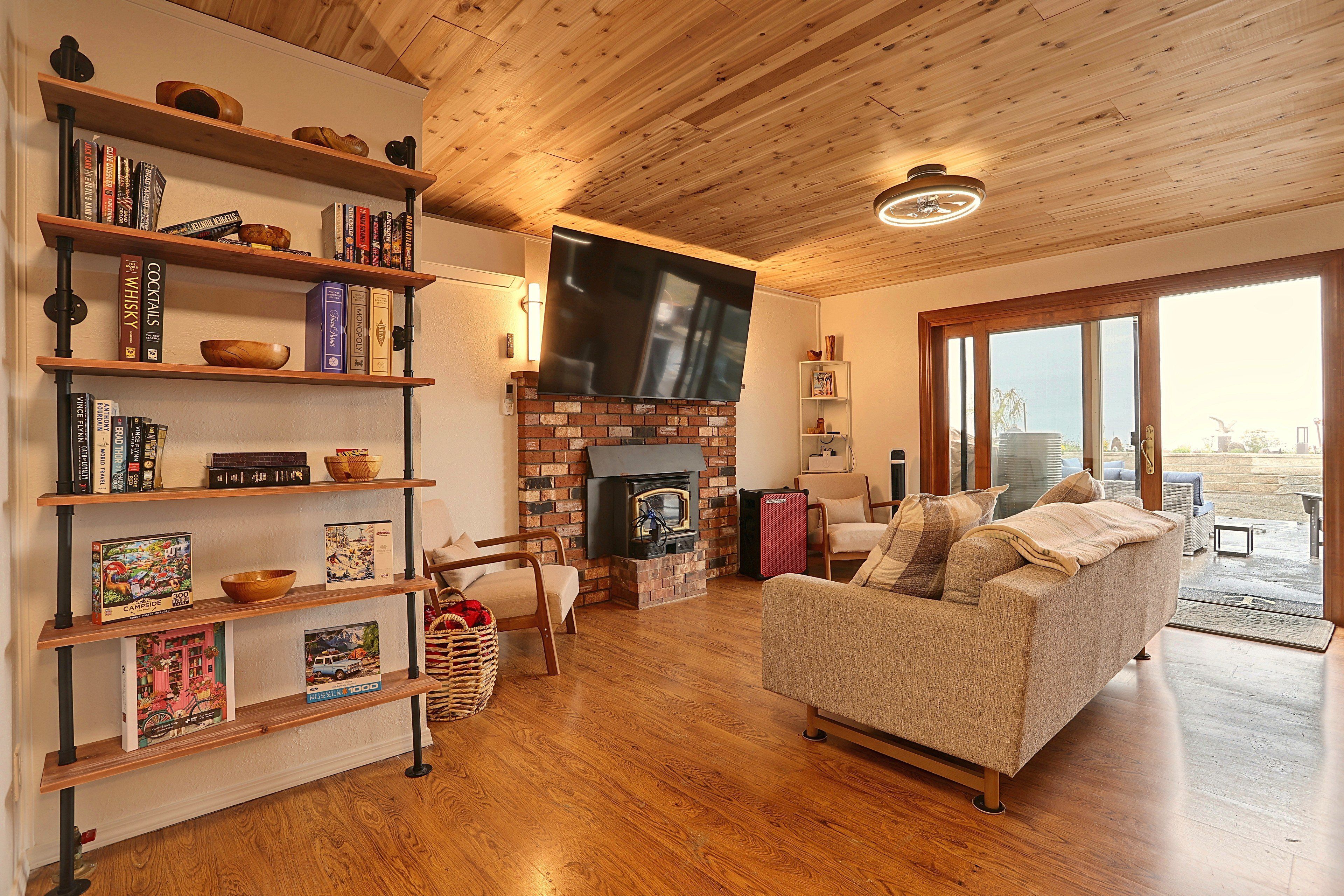 A cozy living room with a fireplace, wooden floors, a flat-screen TV, and a bookshelf filled with books.
