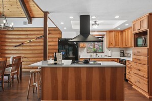 A modern kitchen with wooden cabinetry, a central island, and a black range hood. - Cabin & Guest House Near Sandy River Trails! (Brightwood)
