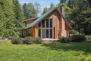 Een vakantiehuis van hout met een grote glazen deur, omgeven door een verzorgd gazon en dicht bos.