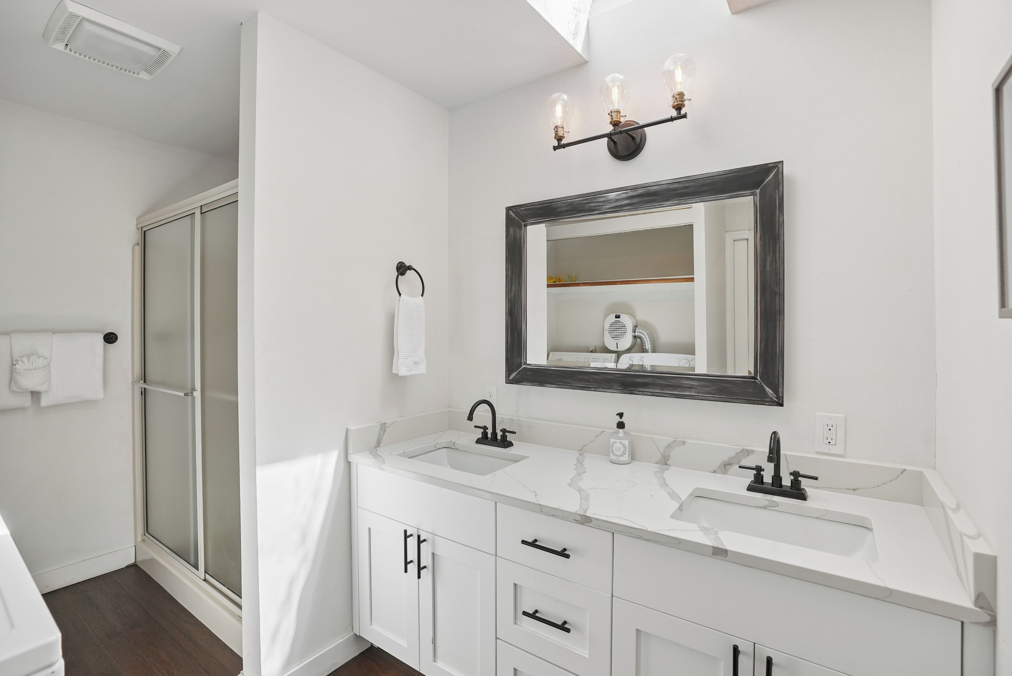 A modern bathroom with a double sink vanity, a large mirror, and a shower area.