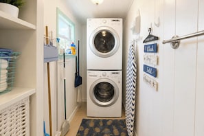 A laundry room with two stacked front-loading washing machines, a drying rack, and a wall-mounted drying rack with labels for different stages of laundry. - 'paradise Found' on Lake Louisa: Swim + Fish! (Clermont)