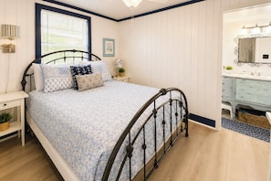 A bedroom with a bed, bedside tables, a window with blinds, a mirror, and a bathroom with a sink and vanity. - 'paradise Found' on Lake Louisa: Swim + Fish! (Clermont)