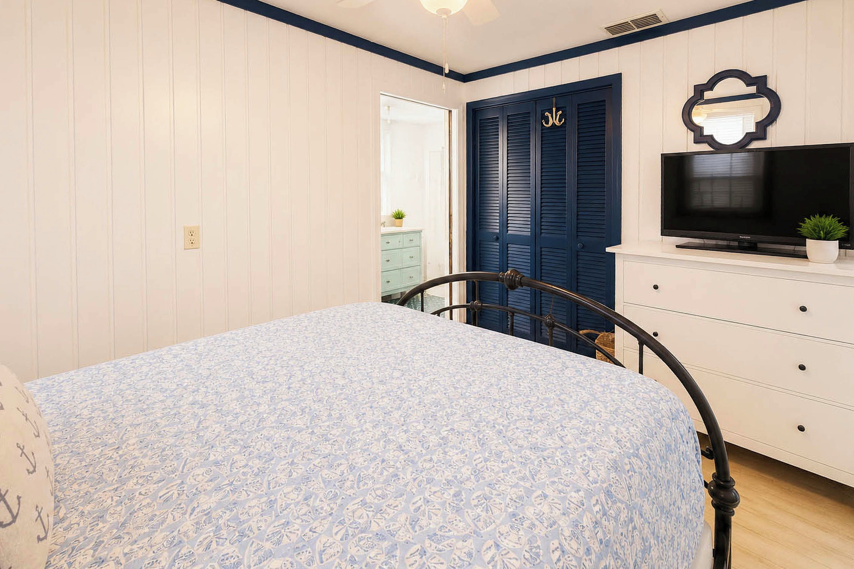 Ein Schlafzimmer mit einem Bett, einem Fernseher auf einer Kommode und einer Tür mit Fensterläden.