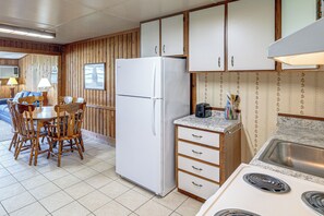 Een kleine keuken met een koelkast, kookplaat en een eethoek met houten meubels.