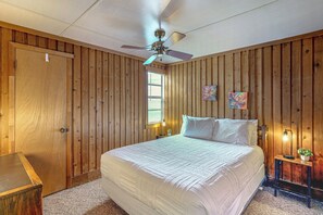 A bedroom with a bed, a ceiling fan, wooden walls, a window, and two wall-mounted lamps. - 'lake Life' Retreat in Clermont w/ Pool & Pier (Clermont)