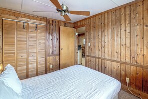 Een slaapkamer met een bed, houten wanden, een plafondventilator en een deur naar een andere kamer.