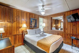 Una camera d'albergo con un letto, una ventola a soffitto, un quadro, una televisione e pannelli in legno.