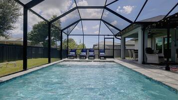 Una piscina con zona cubierta, sillas de descanso y un patio con mobiliario exterior.