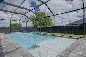 A swimming pool with a clear blue water surface, surrounded by a covered area with a metal frame and a dark fence. - Florida Sunshine! Cape Coral Home w/ Pool (Cape Coral)