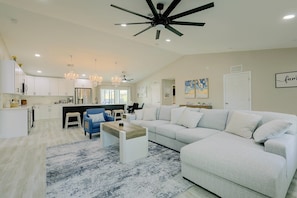 A modern living room with a large sectional sofa, a coffee table, and a chandelier. - Florida Sunshine! Cape Coral Home w/ Pool (Cape Coral)