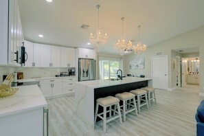 A modern kitchen with white cabinetry, a central island with bar stools, and a chandelier. - Florida Sunshine! Cape Coral Home w/ Pool (Cape Coral)