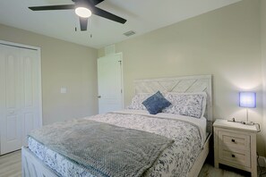 A bedroom with a bed, nightstand, lamp, ceiling fan, and a door. - Florida Sunshine! Cape Coral Home w/ Pool (Cape Coral)