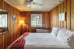 A wooden-paneled room with a bed, a desk, a lamp, a window, and a ceiling fan. - License to Chill: Lake Access, 14 Mi to Disney (Clermont)