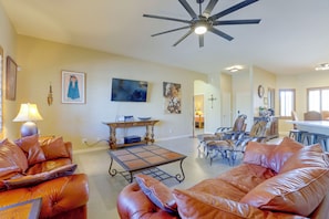 A spacious living room with leather sofas, a ceiling fan, a television, and artwork on the walls. - Desert Hills Fenced Acre! Pool, Spa + Dogs Allowed (Phoenix)