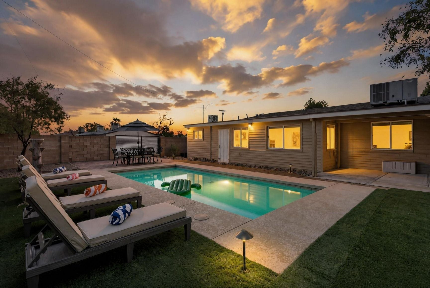 A residential backyard with a swimming pool, lounge chairs, and a patio table.