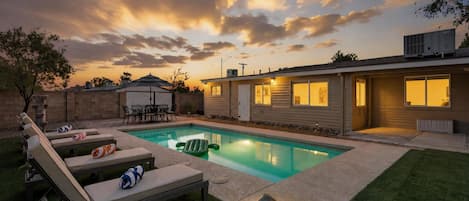 A residential backyard with a swimming pool, lounge chairs, and a patio table.