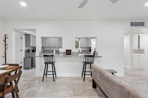 A modern kitchen with a central island, two bar stools, a bench, and a dining table with chairs. - Casa Ebenezer | 4BR Pool & Spa Near Old Town (Scottsdale)