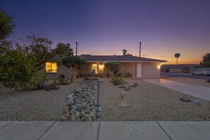 A modern house with a gravel driveway, a small garden with rocks and plants, and a clear sky at dusk. - Casa Ebenezer | 4BR Pool & Spa Near Old Town (Scottsdale)