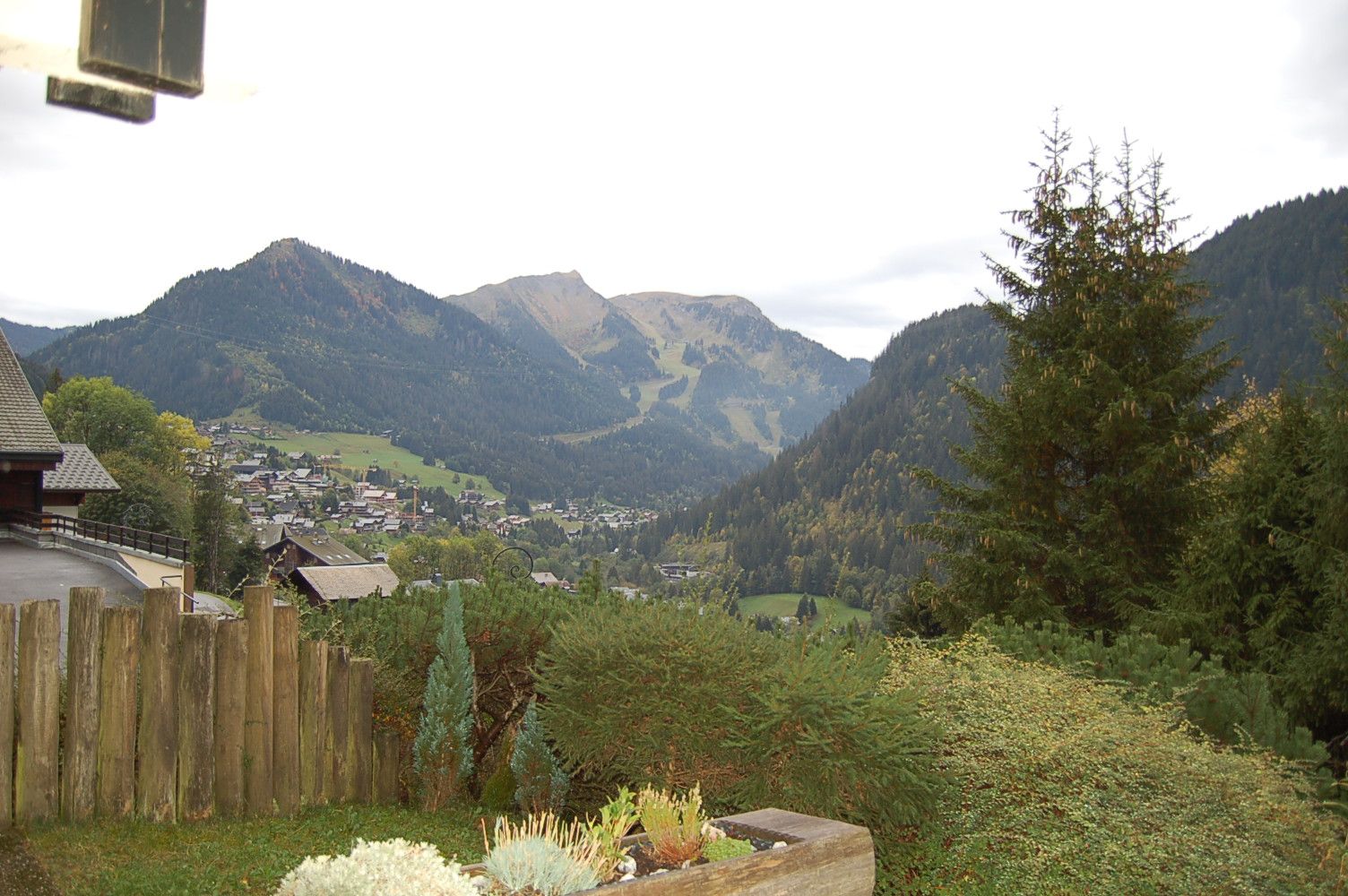 A mountainous landscape with a village in the valley, wooden fence, and a variety of vegetation.