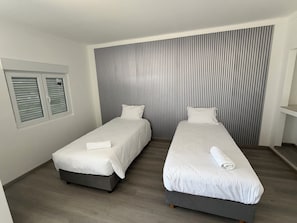A hotel room with two single beds, a window with blinds, and a striped wall. - Alojamento Local Cova Da Serpe (Figueira da Foz)