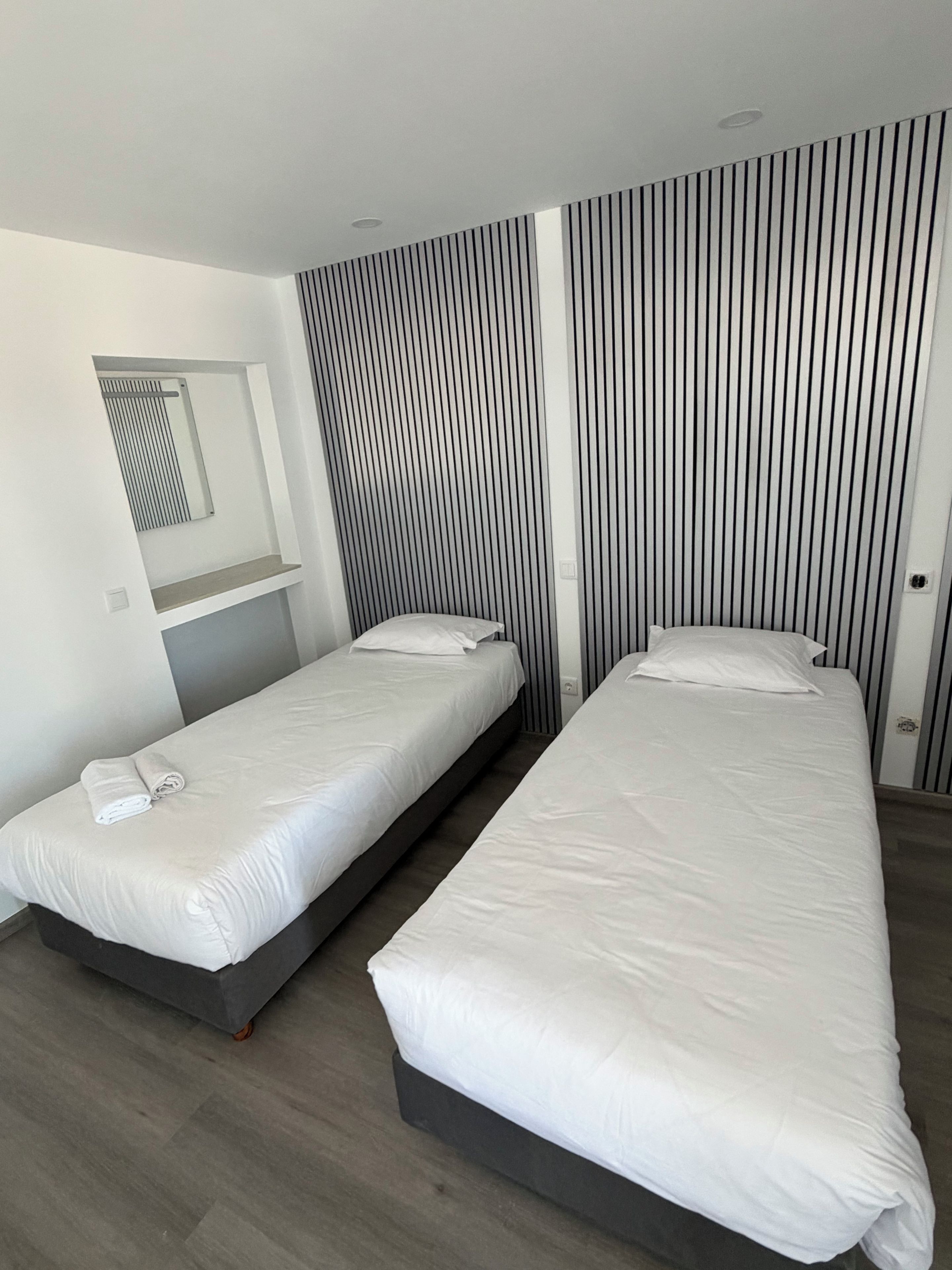 Een moderne slaapkamer met twee eenpersoonsbedden, een inbouwkbank en een verticaal gestreept wandontwerp.