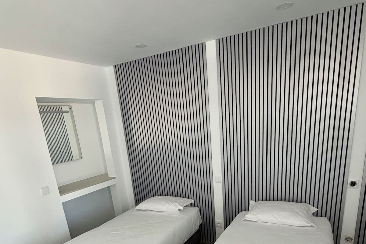 A modern bedroom with two single beds, a built-in bench, and a vertical striped wall design.