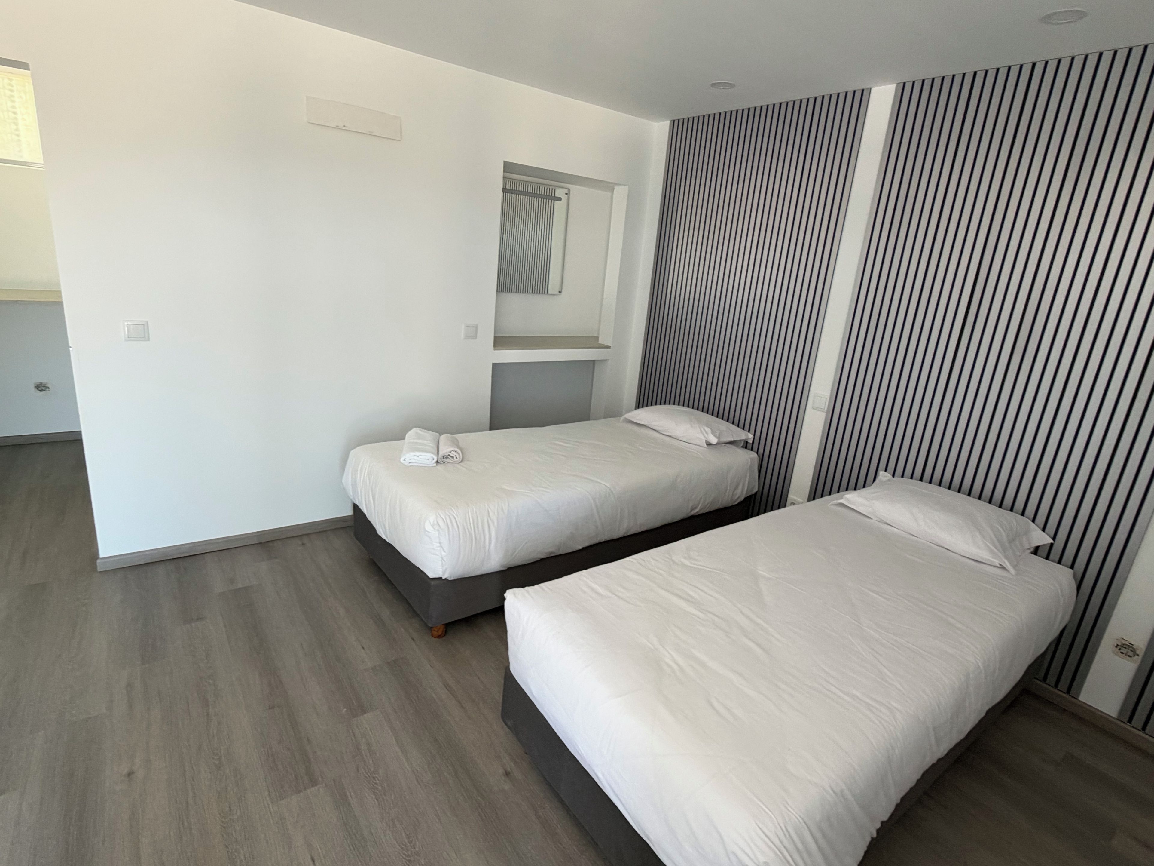 A modern hotel room with two single beds, a large mirror, and a striped wall.