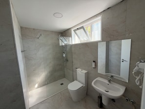 A bathroom with a shower, toilet, sink, and a window providing natural light.