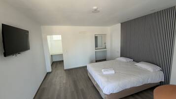 Habitación de hotel moderna con una cama grande, un televisor de pantalla plana en la pared, un pequeño rincón de descanso y un baño con espejo.