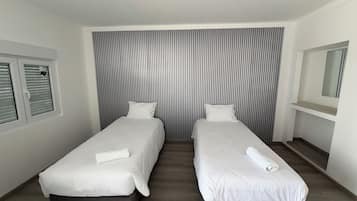 Une chambre d’hôtel avec deux lits simples, une fenêtre avec des stores, un miroir et un mur à rayures.