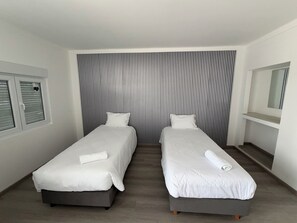 A hotel room with two single beds, a window with blinds, a mirror, and a striped wall. - Alojamento Local Cova Da Serpe (Figueira da Foz)