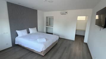 Une chambre moderne avec un grand lit, une armoire intégrée, un téléviseur et une salle de bain visible à travers une porte ouverte.